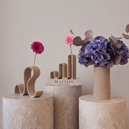 Colecția Vernisaj în crem texturat, vaze decorative Antiform cu forme ondulate, gerbera roz și aranjament de hortensii